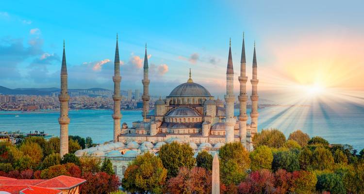 Historic mosque with multiple minarets overlooking the water at sunset.