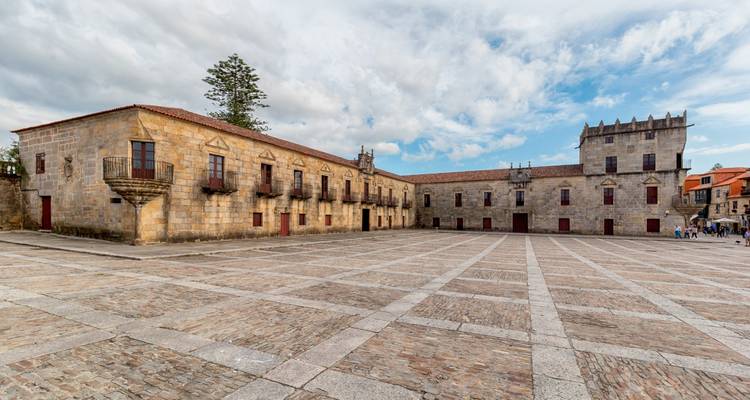 Cour en pierre avec bâtiments historiques et un ciel nuageux.