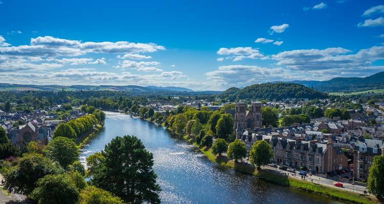 Vue sur la rivière avec des bâtiments et des arbres bordant les rives sous un ciel dégagé.