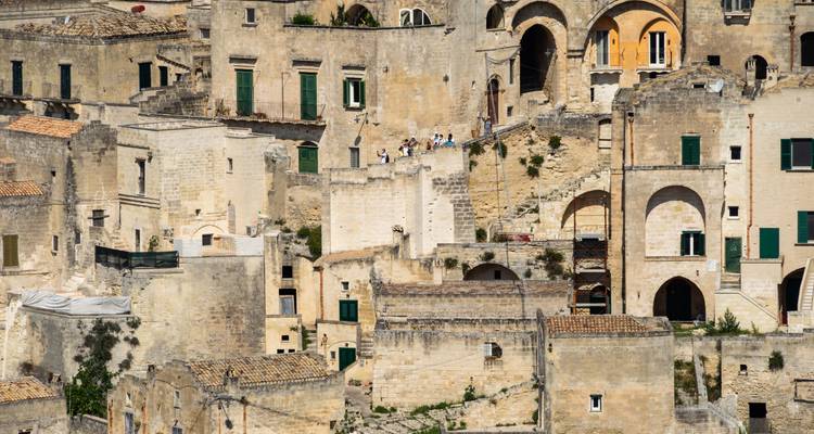 A close-up of ancient buildings in Matera, Italy, with people touring the area.