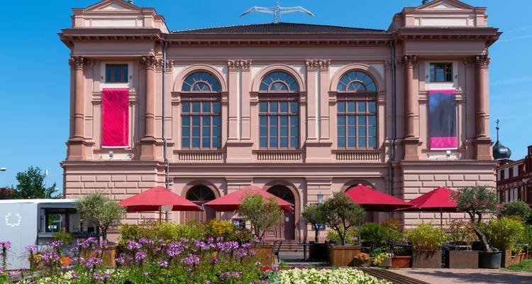 Façade d'un bâtiment classique avec de grandes bannières et des sièges extérieurs.