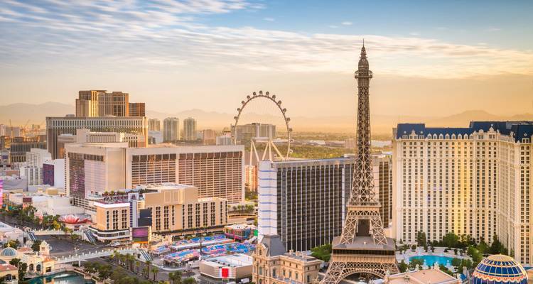 Sun-lit view of Las Vegas resort towers with replica Eiffel Tower and High Roller observation wheel.