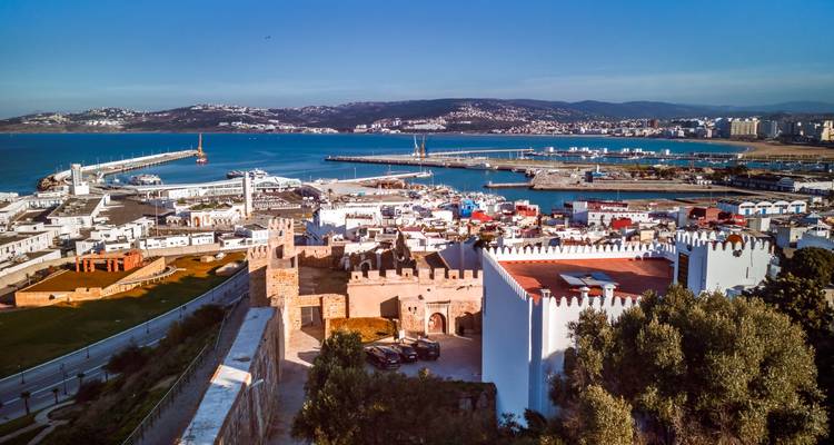 A coastal cityscape with fortifications overlooking a harbor, likely Tangier, Morocco.