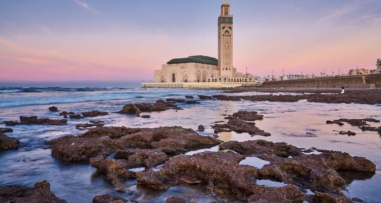 A mosque situated by the sea during sunset, likely Hassan II Mosque in Casablanca, Morocco.