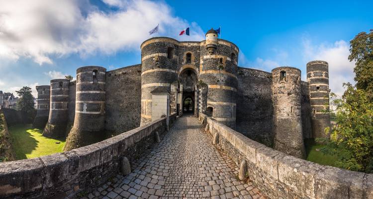 Historic stone fortress with rounded towers and flags above.