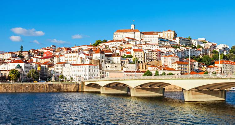 Cityscape of Coimbra with historical buildings and a bridge over a river.