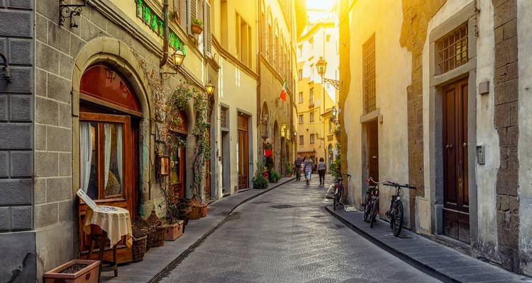 Une rue étroite pittoresque en Italie avec des magasins et des vélos au coucher du soleil.