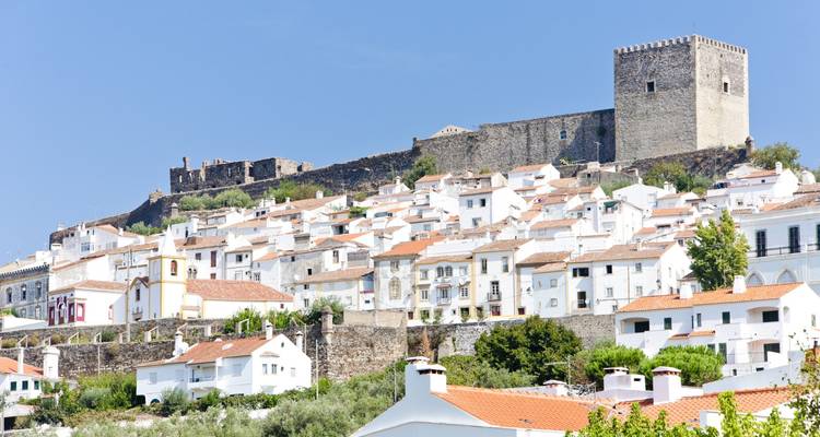 Bâtiments blancs et rustiques empilés sur une colline avec une forteresse.