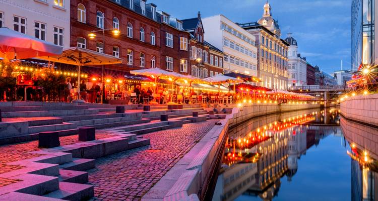 Paseo iluminado junto al canal con luces reflejándose en el agua.