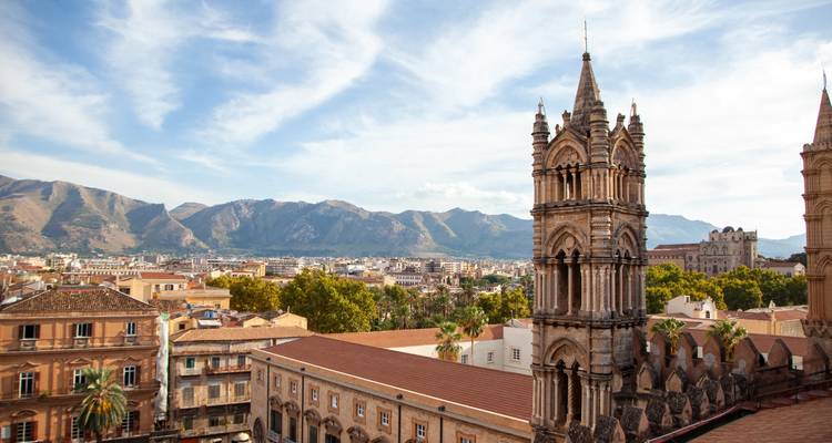 Panoramic city view with cathedral towers and surrounding mountains.
