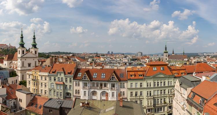 Escena panorámica de los coloridos tejados de Brno, edificios ornamentados y campanarios de iglesias bajo un cielo soleado.