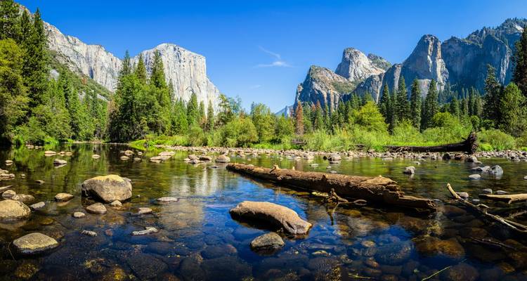 Rivière cristalline reflétant les falaises de granit et les forêts de pins dans la vallée de Yosemite sous un ciel bleu éclatant.