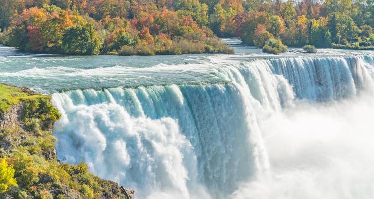 Puissant rideau des chutes du Niagara plongeant dans la brume avec des arbres d'automne colorés bordant les rives.