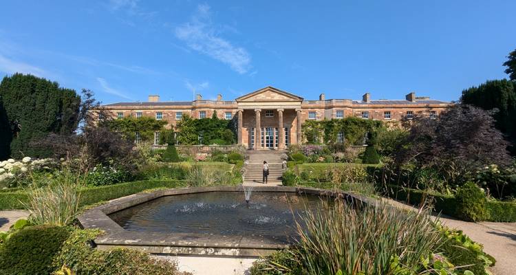 Une grande demeure historique avec un jardin à la française et une fontaine.