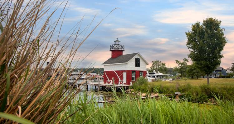 Charming red lighthouse cottage near a marina surrounded by reeds at sunset in Saugatuck.