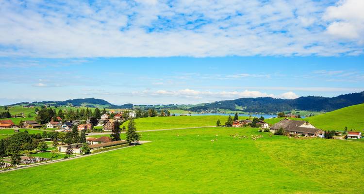 Wide green fields with scattered homes and a distant lake.