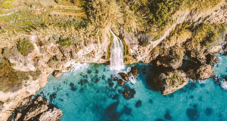Aerial view of a waterfall cascading into blue ocean water.
