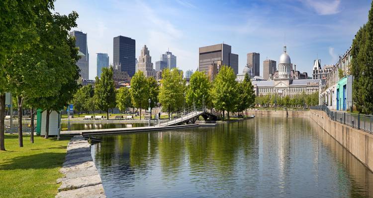 Calm canal reflects the historic domed market building and modern skyline of Montreal under blue skies.