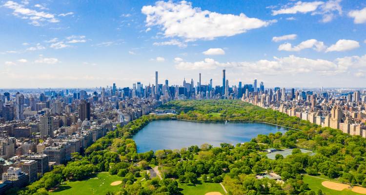 Aerial panorama of Central Park’s reservoir with Manhattan’s skyline under bright skies.