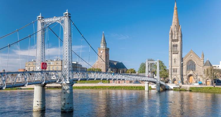 Pont suspendu avec église historique et bâtiments au bord de la rivière.
