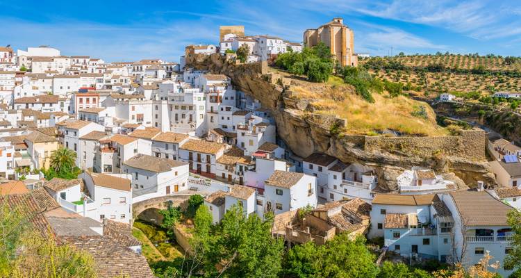 A picturesque town built into rocky cliffs, with white homes and greenery surrounding the area.