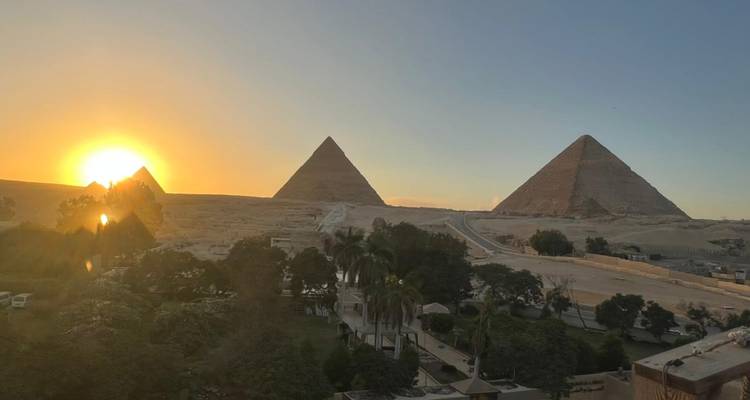 Las Pirámides de Giza al atardecer con árboles y desierto en silueta.