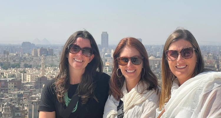 Tres mujeres posando con un paisaje urbano y pirámides en la distancia.