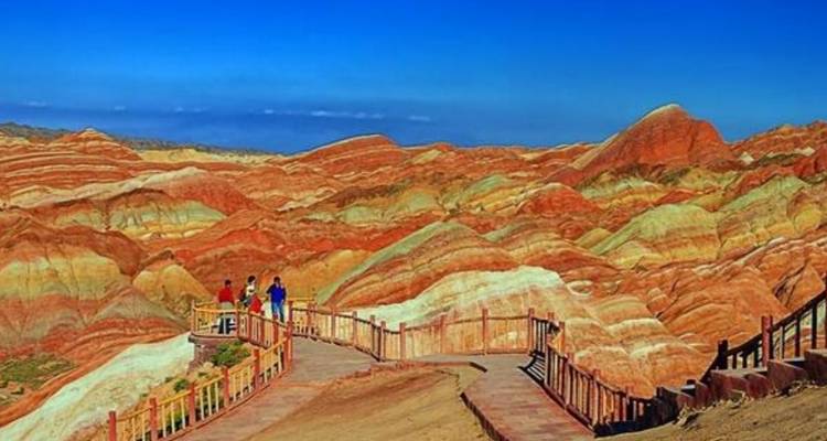 People walking along a boardwalk with colorful rock formations in the background.