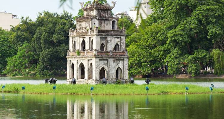 Tour ancienne sur une île au milieu d'un lac entourée de verdure.