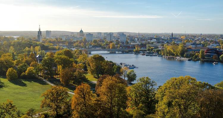 Une vue panoramique sur la rivière Havel de Potsdam encadrée par des arbres d'automne et un horizon urbain lointain.