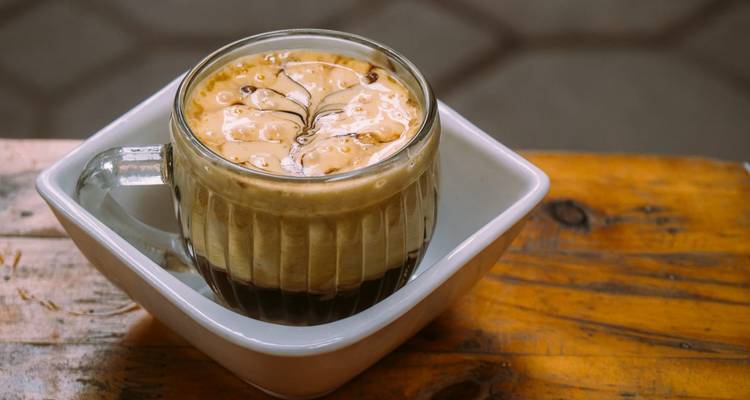 Une tasse de café aux œufs avec un motif artistique de mousse servie sur une table en bois.