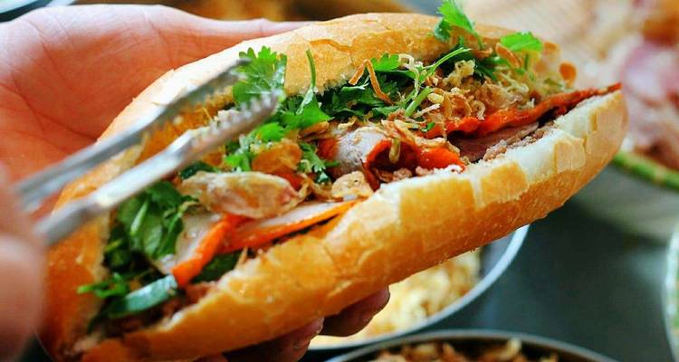 Gros plan d'un sandwich banh mi tenu avec des pinces.