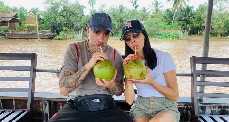 Un couple assis sur un bateau buvant dans des noix de coco avec des pailles.