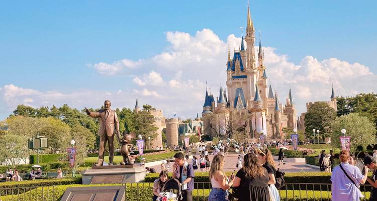 Statue et château dans un parc à thème avec des visiteurs qui se promènent.