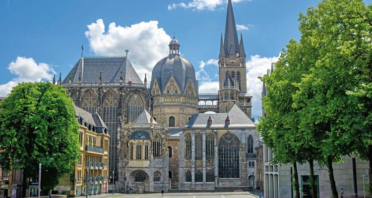Aachener Dom mit blauem Himmel und grünen Bäumen.