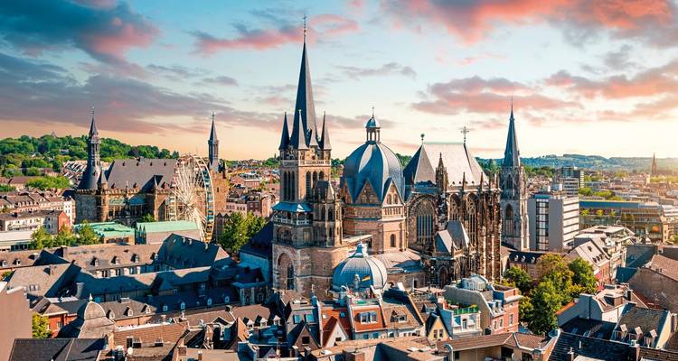 Luftaufnahme von Aachen mit dem Dom im Zentrum und farbenfrohem Sonnenuntergang.