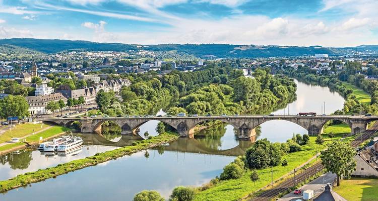 Eine Brücke mit Blick auf einen Fluss mit grünen Landschaften und einer Stadt im Hintergrund.
