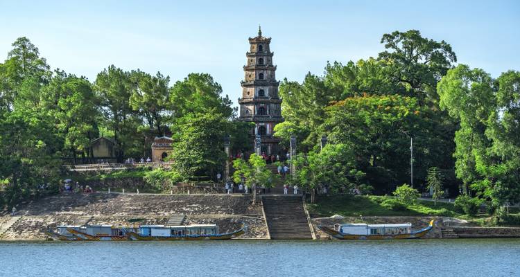 Pagode au bord d'une rivière avec des bateaux amarrés.