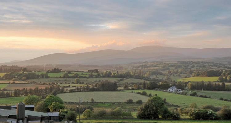 Coucher de soleil sur des collines vallonnées et des champs dans une zone rurale.