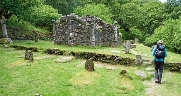 Personne explorant d'anciennes ruines avec des pierres tombales entourées d'arbres.