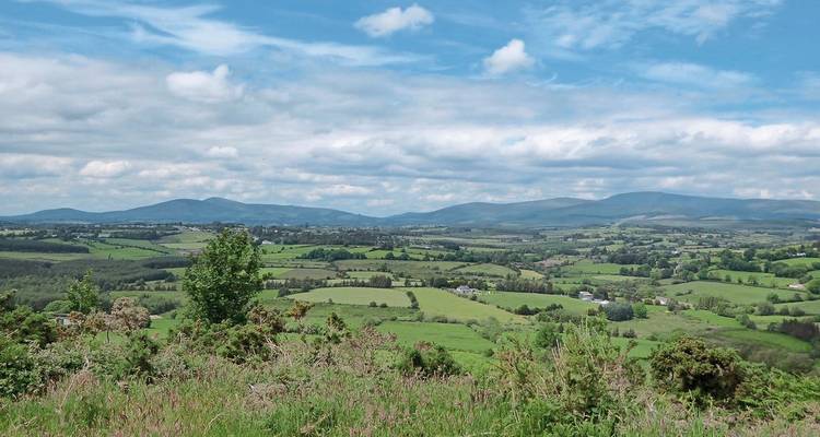 Vista expansiva de campos verdes y colinas bajo un cielo azul.