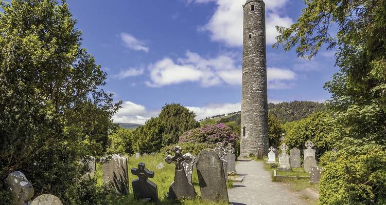 Antigua torre redonda rodeada de lápidas y árboles.