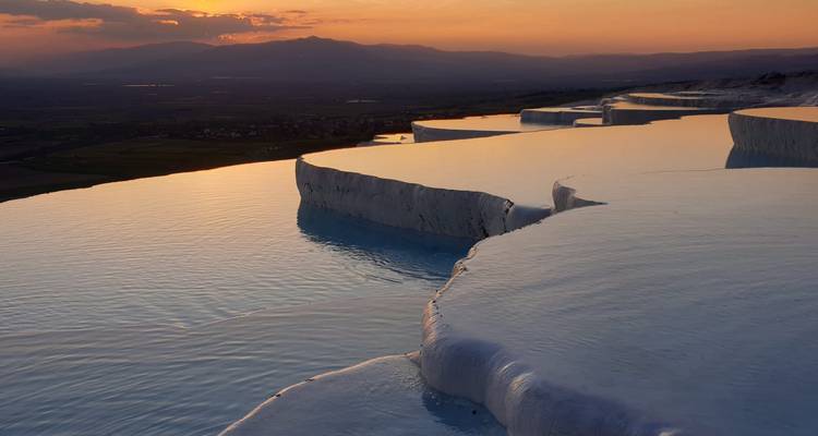 Terraced thermal pools with sun setting in the background.
