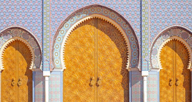 Arches carrelées de mosaïques colorées et portes dorées finement sculptées d'un palais marocain.