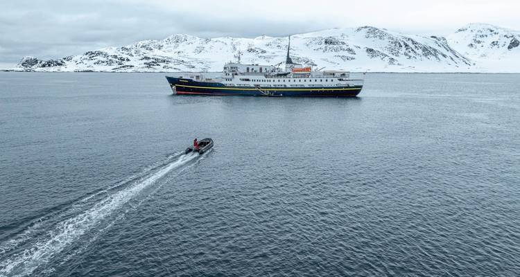 Bateau avec des gens sur la mer, montagnes enneigées en arrière-plan.