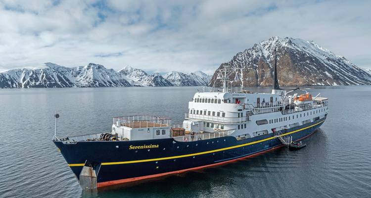 Navire nommé Serenissima sur l'eau avec des montagnes enneigées en arrière-plan.
