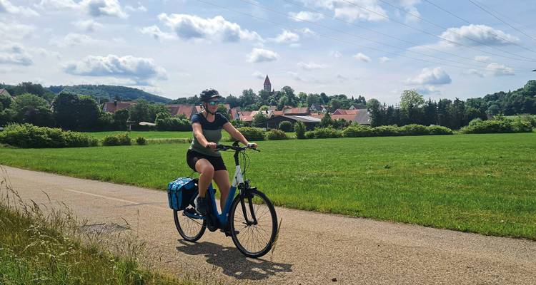 Een fietser op een pad in een landelijk gebied met gebouwen in de verte.