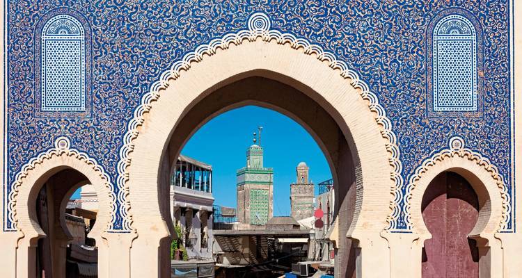 Ein verzierter Bogen mit blauen Mosaikfliesen, der den Blick auf ein Minarett rahmt.