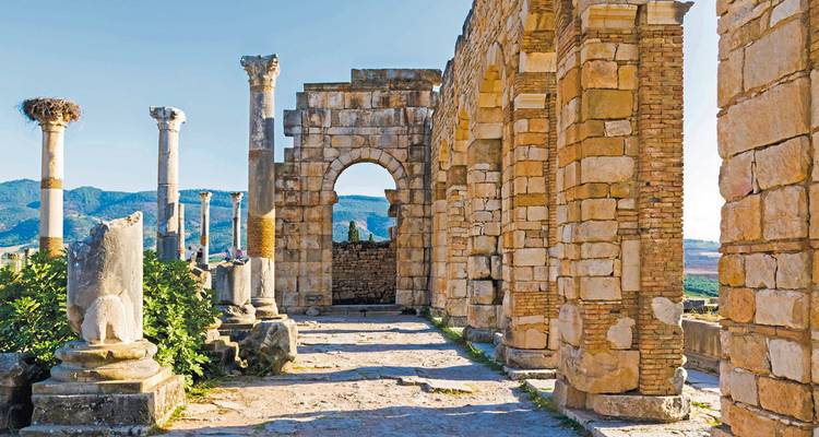 Antike Steinruinen mit Bögen und einer bergigen Kulisse.