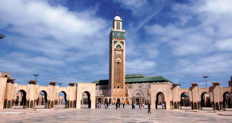 Große Moschee mit belebtem Innenhof unter blauem Himmel.
